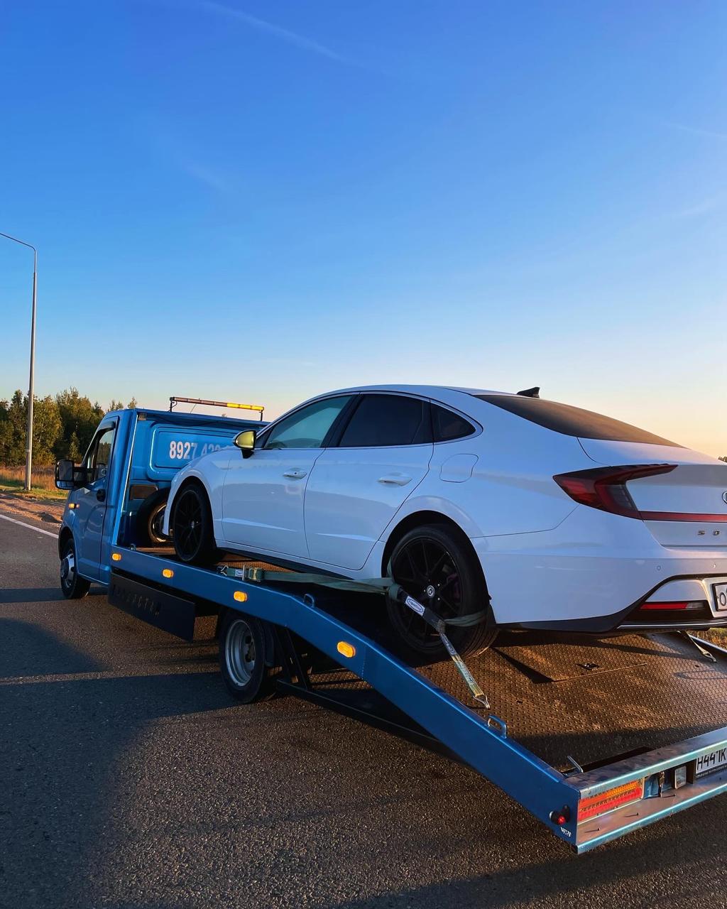 Белый седан на эвакуаторе на трассе при закате